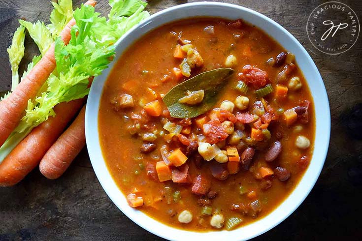 The finished Minestrone Soup Recipe served in a white bowl with fresh carrots and celery laying next to the bowl.