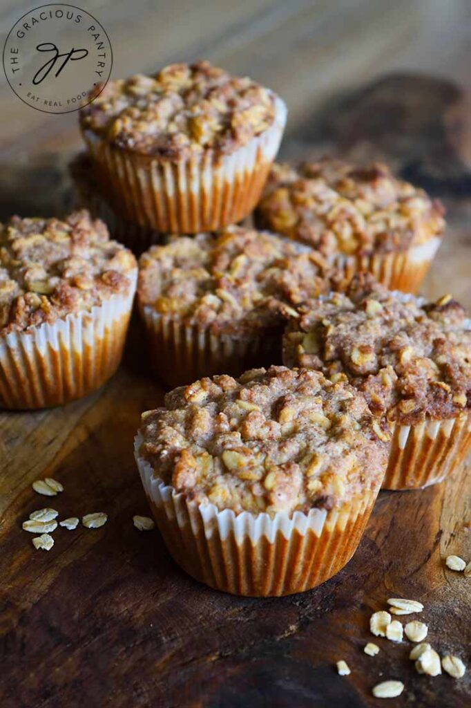 Seven Oat Flour Muffins With Streusel Topping sitting on a cutting board with raw oats sprinkled around the board.