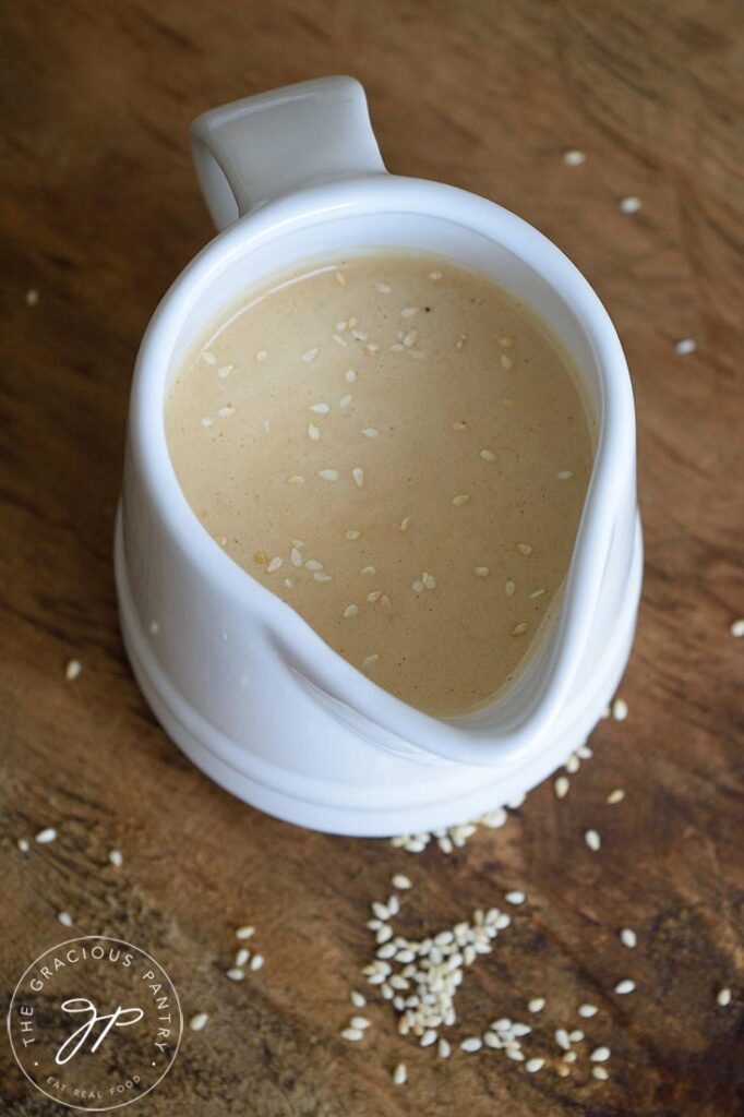 Side view of a small, white pitcher filled with Sesame Vinaigrette. Sesame seeds are sprinkled over the top.