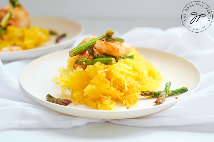 The finished Shrimp And Asparagus Spaghetti Squash Spaghetti, served on a white plate.