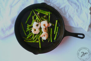 Sautéing the shrimp and asparagus in a cast iron pan.