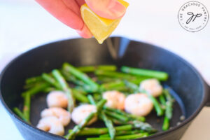 Squeezing the lemon juice over the shrimp and asparagus in a cast iron skillet.