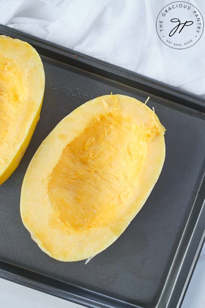 Raw, cut spaghetti squash, cut in half and placed on a baking pan for baking.