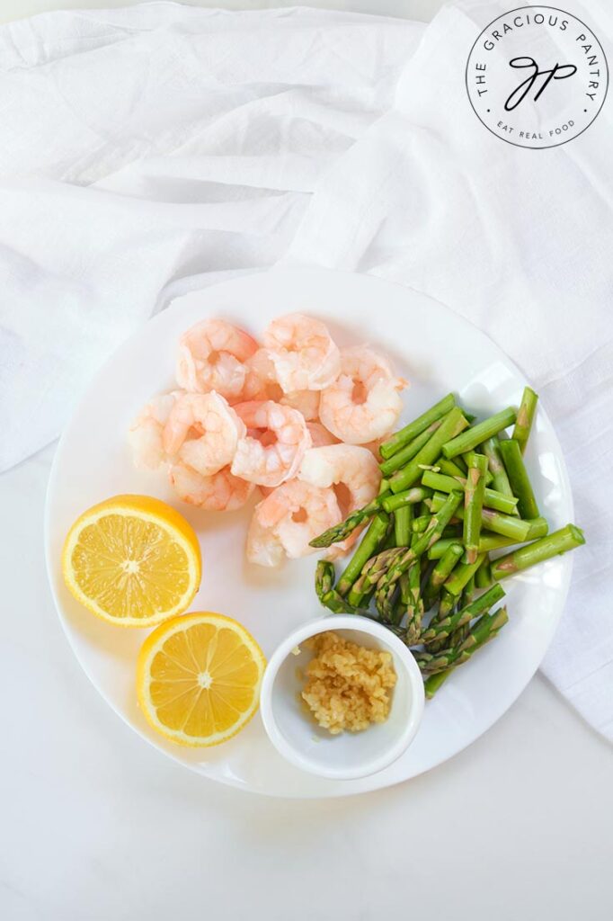 The rest of the recipe ingredients, sitting on a plate, waiting to be used in this Shrimp And Asparagus Spaghetti Squash Spaghetti Recipe. Shrimp, fresh lemon, minced garlic and cut asparagus.