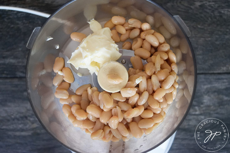The beans and the mayo sitting in a food processor, waiting to be blended to make this Healthy Spinach Artichoke Dip Recipe