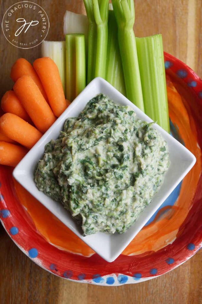 The finished Healthy Spinach Artichoke Dip in a serving dish with baby carrots and celery sticks on a colorful plate.
