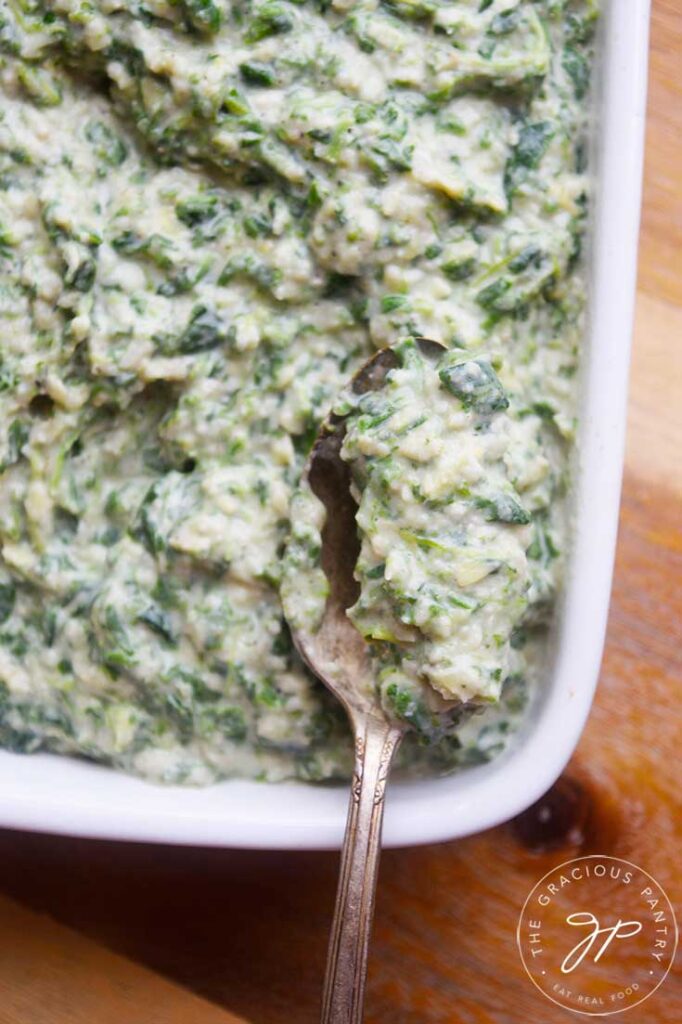 A spoon filled with this Healthy Spinach Artichoke Dip being lifted towards the camera.