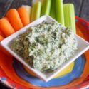 A side view of the served Healthy Spinach Artichoke Dip with carrots and celery sticks sitting just behind it.