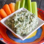 A side view of the served Healthy Spinach Artichoke Dip with carrots and celery sticks sitting just behind it.