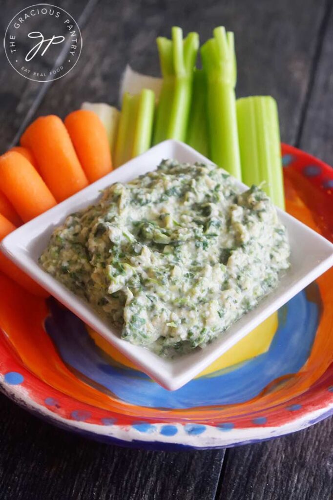 A side view of the served Healthy Spinach Artichoke Dip with carrots and celery sticks sitting just behind it.