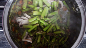 Adding the mushrooms and asparagus to the pot.