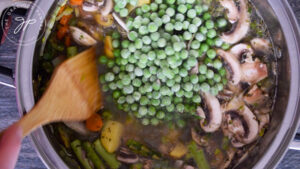 Adding the peas and diced tomatoes to the Spring Minestrone Soup pot.