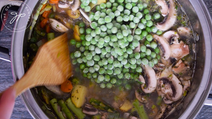 Adding the peas and diced tomatoes to the Spring Minestrone Soup pot.