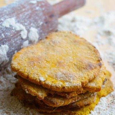 A stack of this Sweet Potato Flatbread sits on a floured surface, next to a floured rolling pin.