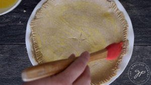 Brushing an egg wash onto the top crust just before baking.