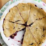 An overhead view of a whole blueberry pie with a single slice removed.