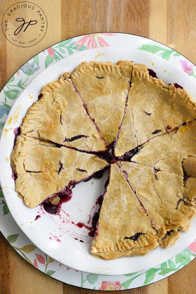 An overhead view of a whole blueberry pie with a single slice removed.