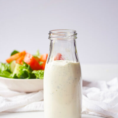 The finished Buttermilk Ranch Dressing in a dressing bottle with a salad sitting behind it.