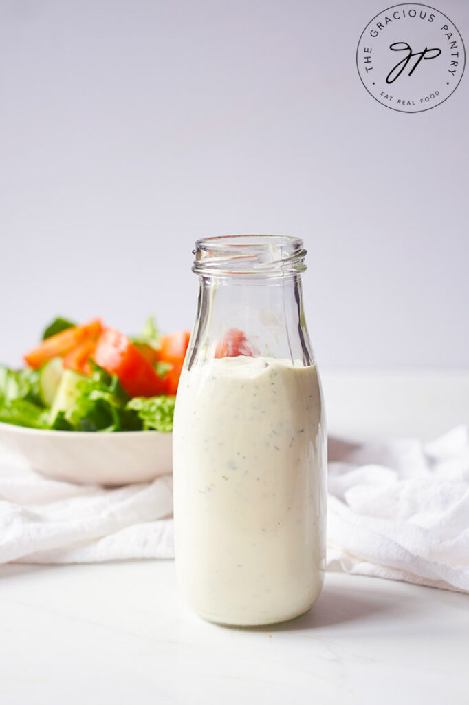 The finished Buttermilk Ranch Dressing in a dressing bottle with a salad sitting behind it.