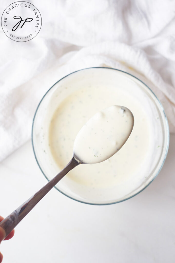 A spoon lifts some of this Buttermilk Ranch Dressing up out of a mixing bowl and towards the camera.