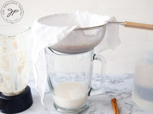 Straining the blended rice through a sieve with a cheesecloth.