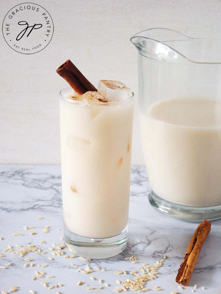 Homemade Horchata in a pitcher and a glass. A cinnamon stick rests in the glass for garnish.