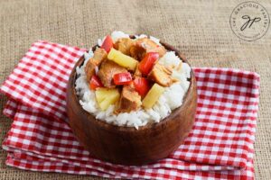 The finished Slow Cooker Pineapple Chicken, served over rice in a wooden bowl. The bowl sits on a red and white checkered towel.