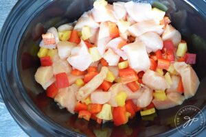 The chicken, peppers and pineapple mixed together in the slow cooker crock.