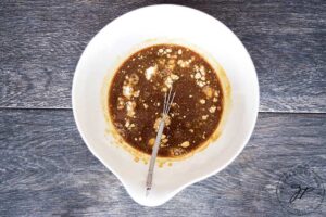 The Slow Cooker Pineapple Chicken sauce being whisked together in a small, white mixing bowl.