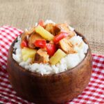 Slow Cooker Pineapple Chicken served in a wood bowl over rice, sitting on a table.