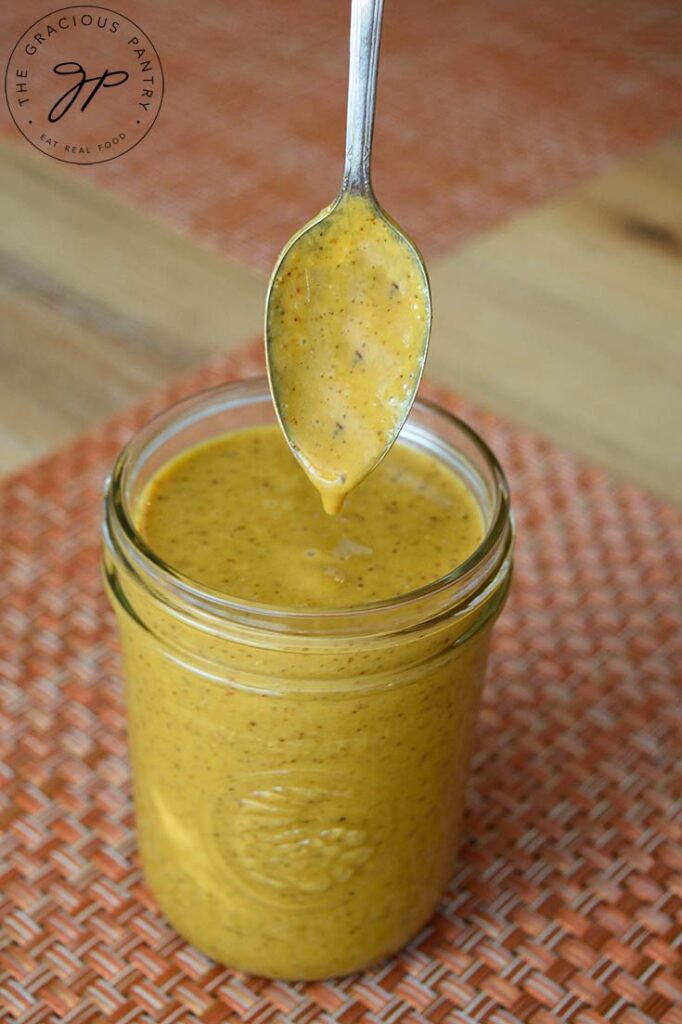 A jar of Carolina Mustard Barbecue Sauce with a spoon just dipped in over the top.