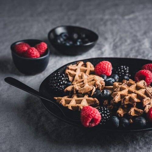 Protein Powder Waffles on a black plate with blackberries and raspberries sprinkled over the top.