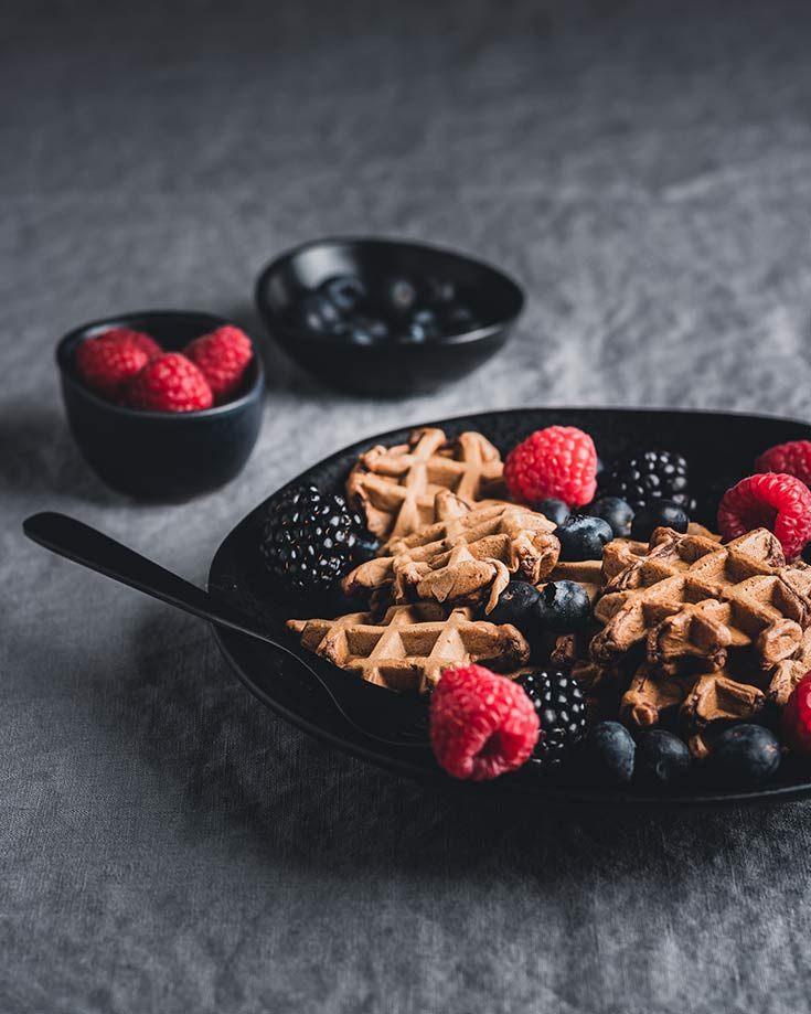 Protein Powder Waffles on a black plate with blackberries and raspberries sprinkled over the top.