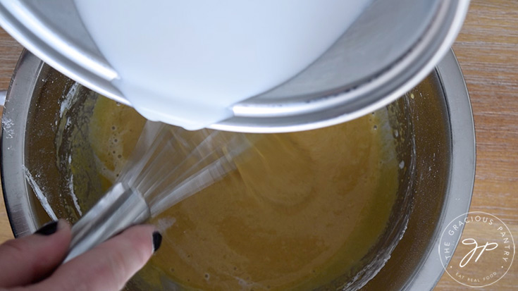 Pouring some of the hot coconut milk into the egg mixture while whisking.