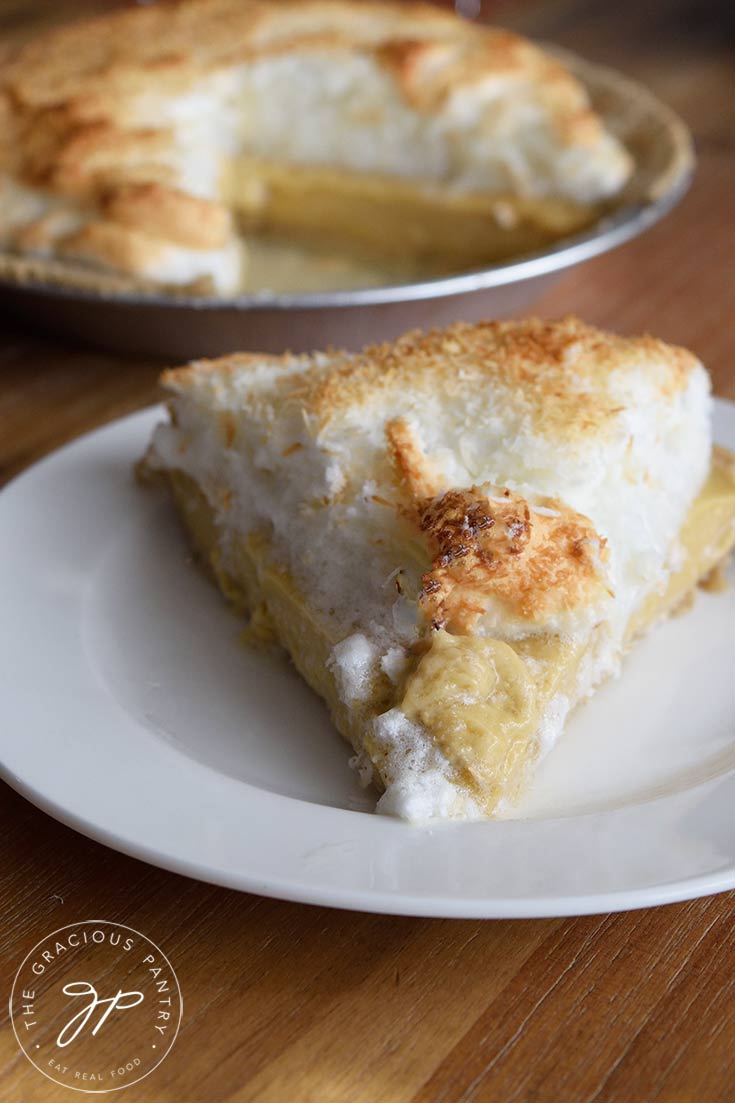 A single slice of Coconut Meringue Pie Recipe on a plate, with the whole pie sitting behind it.