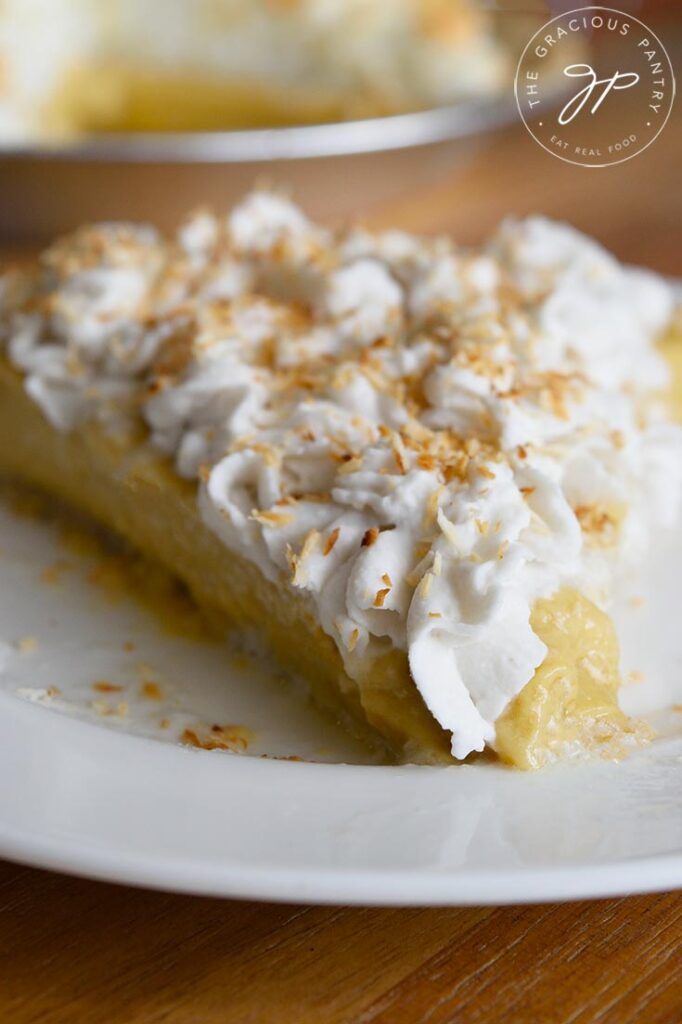 A front view of a single slice of coconut cream pie with roasted cocoanut sprinkled on top.