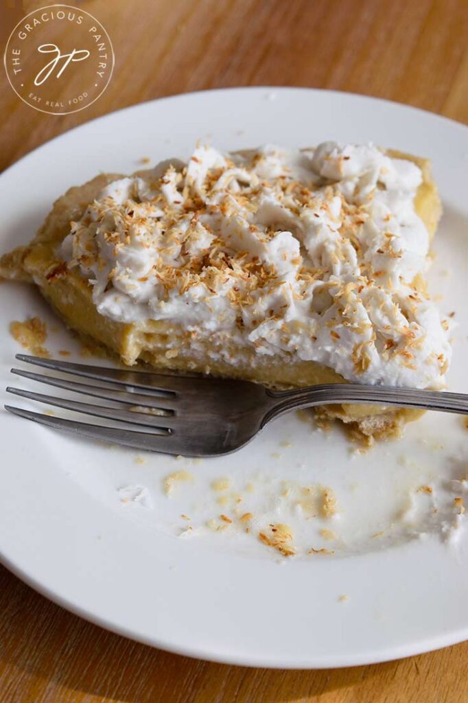 A half eaten slice of coconut cream pie with a fork resting next to the slice on the plate.