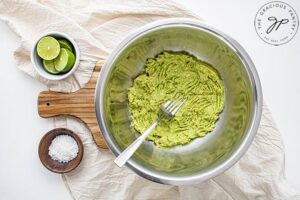 Mashed avocado in a metal mixing bowl.