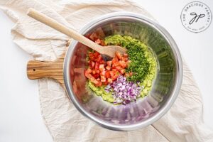 The onion, pepper and tomato added to the mixing bowl of mashed and salted avocado.