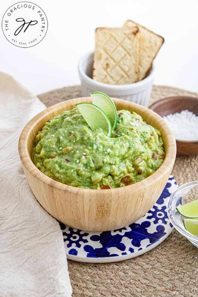 A wooden bowl filled with guacamole. Two lime slices garnish the top.