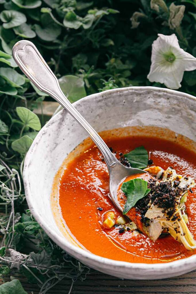 A bowl of gaspacho sits next to some flower showing soup options for this list of Healthy Dinner Recipes.
