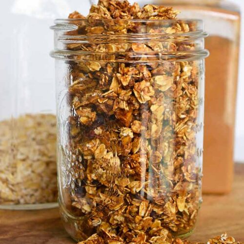An up close shot of granola in a canning jar. A bottle of cinnamon sits behind it.