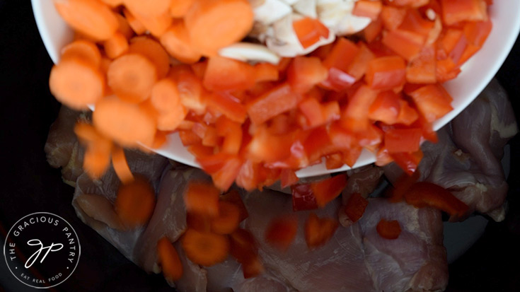 Adding the vegetables to the crock, over the chicken.