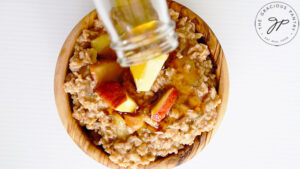 Pouring maple syrup over the finished Apple Pie Oatmeal in a wooden bowl.