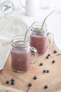 Two glass mugs filled with Acai Smoothie. Fresh berries lay around the base of the jar.