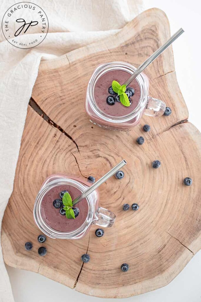 An overhead view looking down into two glass mugs filled with Acai Smoothie and garnished with mint leaves and fresh berries.