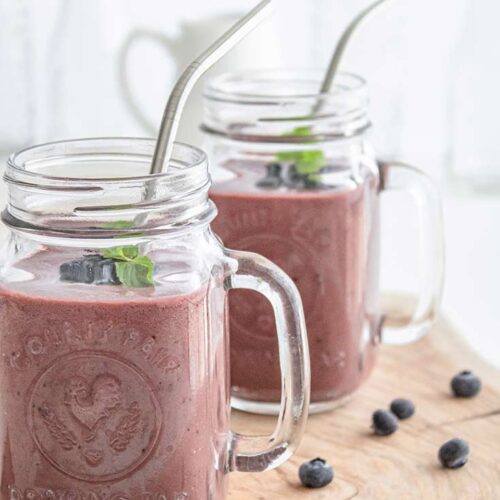 An up close shot of mugs filled with this smoothie and topped with mint leaves and metal straws.