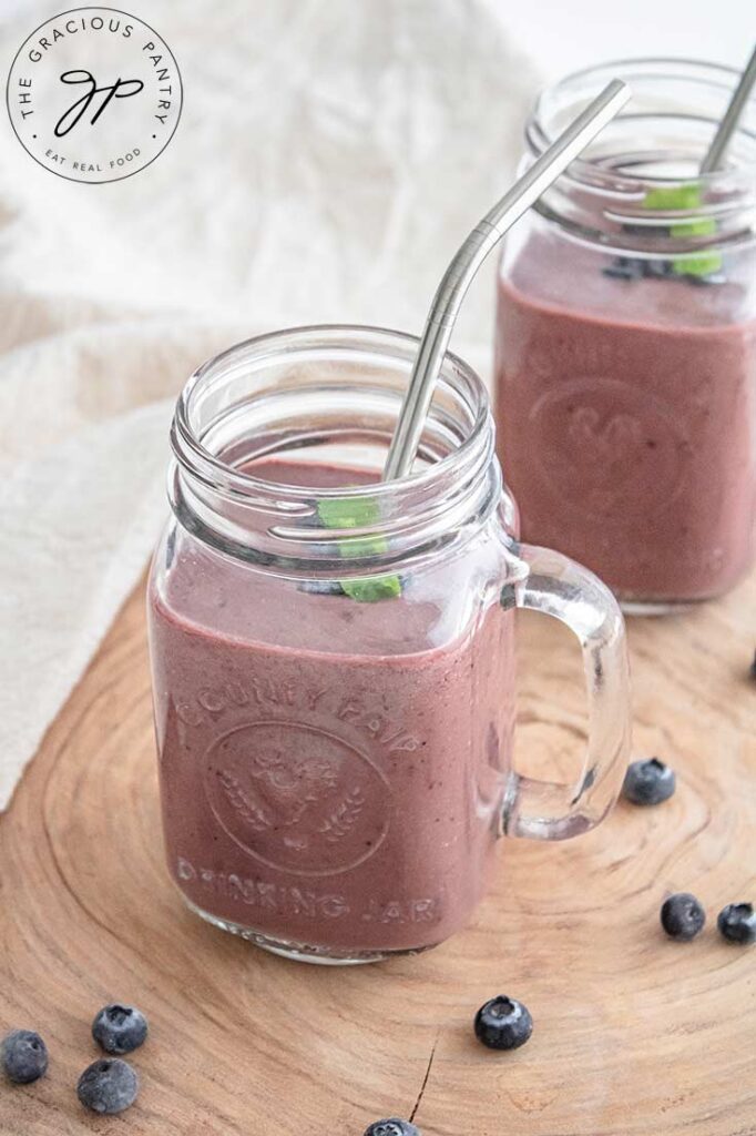 Two glass mugs sit on a wooden surface with a towel behind them, filled with Acai Smoothie.