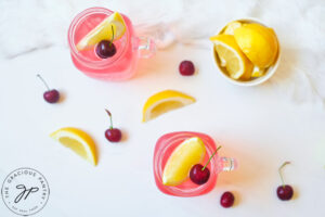 An overhead shot looking down at two glass mugs filled with Cherry Green Tea Lemonade. A small bowl of lemon wedges sits to the side.