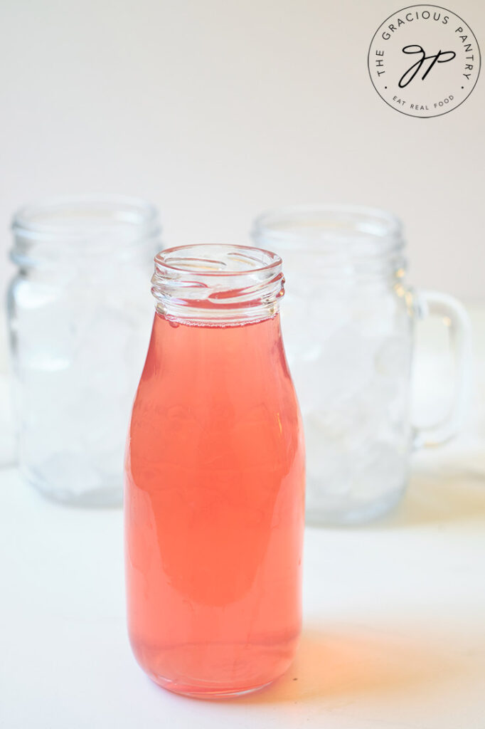 A single glass jar of Cherry Green Tea Lemonade sits in front of two glasses filled with ice.